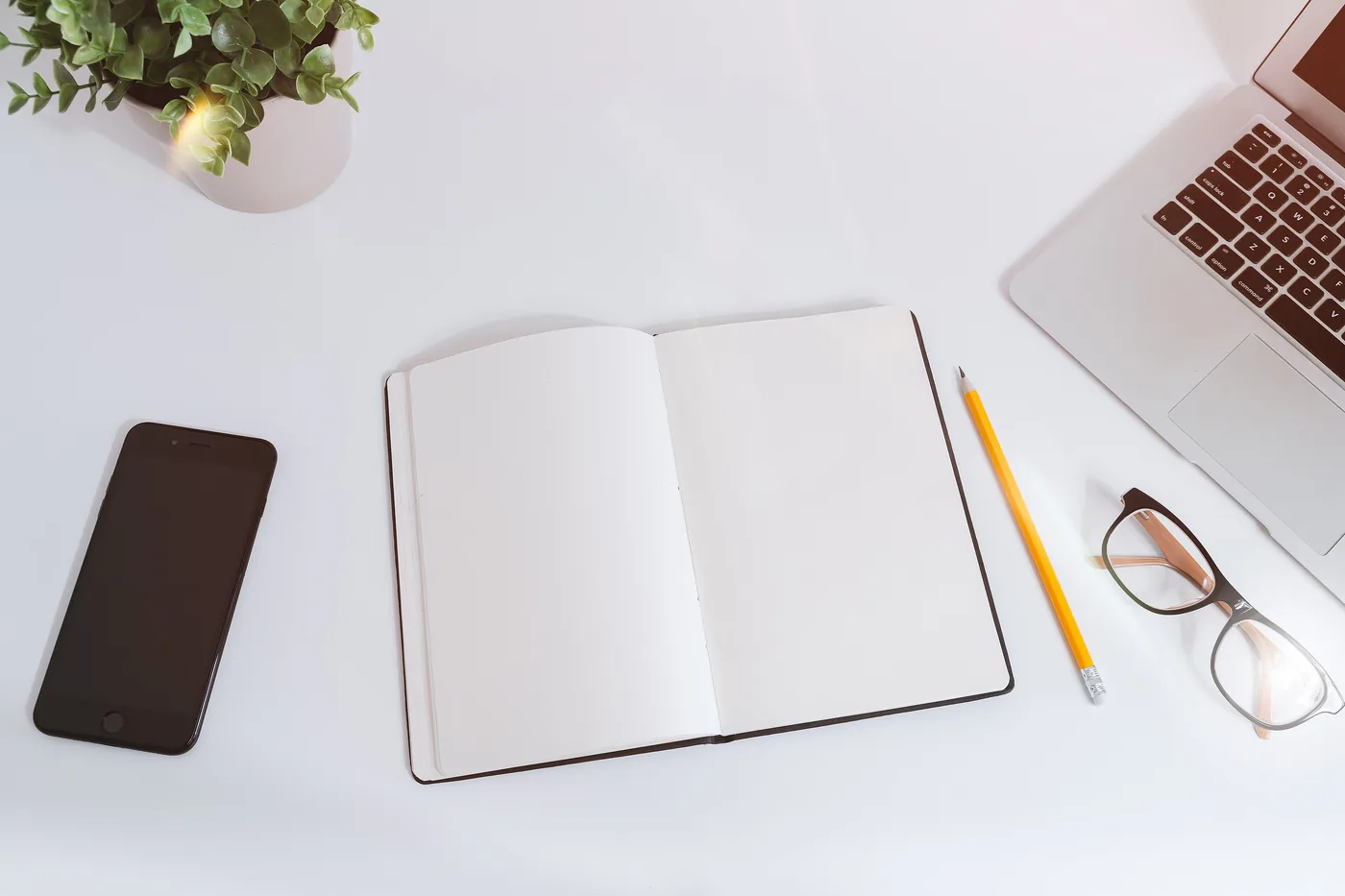 Illustrative photograph: an open notebook, a phone and a pencil laid out on a clean white desk