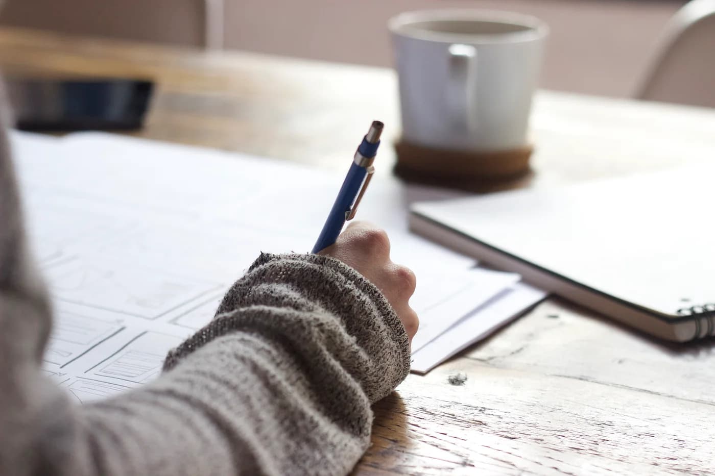 Illustrative planning session: a designer sketching website wireframes on paper beside a notebook and a cup of coffee