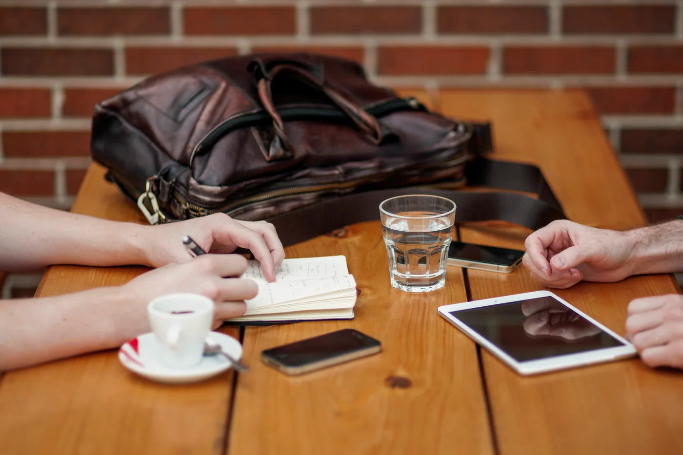 Illustrative discovery meeting: two people at a café table, one taking notes, with a tablet and phones between them