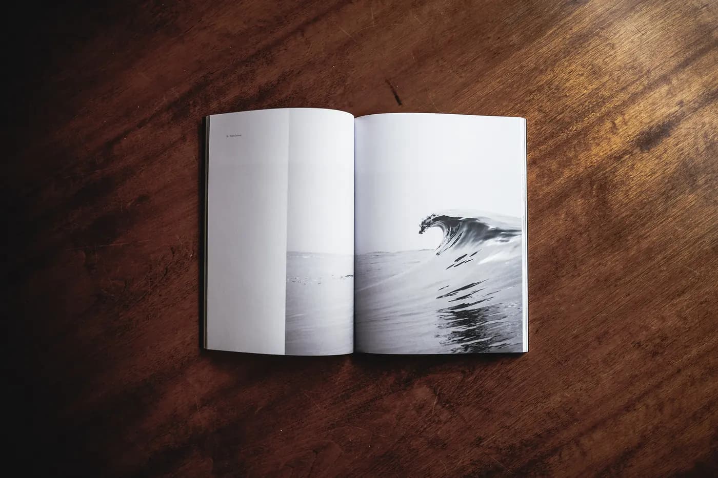 Portfolio concept: an open photography book showing a breaking wave, on a dark wooden table