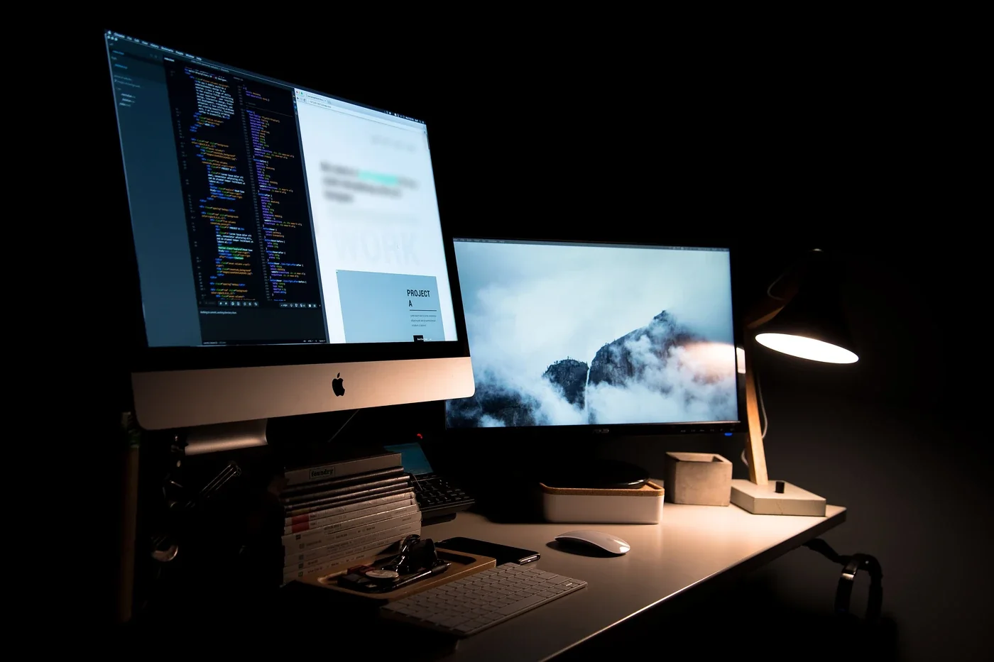 Website development concept: a desktop screen showing code beside a web page in progress, with a second display and a desk lamp